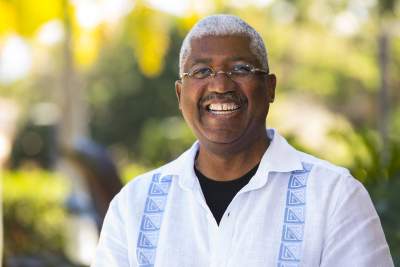 A man with glasses and white hair is smiling.
