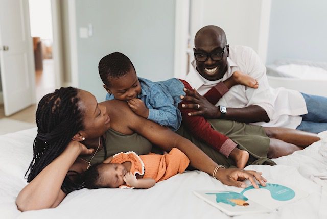 A family laying on the bed with their baby.