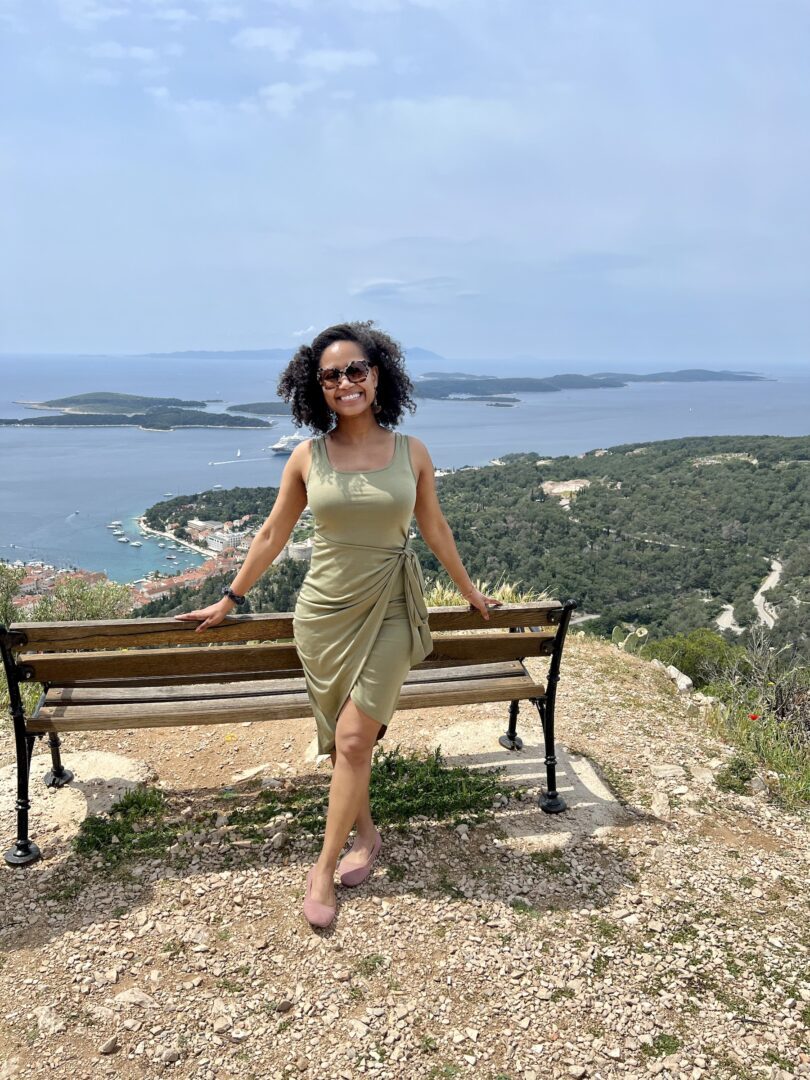 A woman standing on top of a bench near the ocean.
