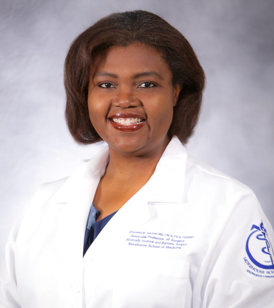 A woman in white lab coat standing next to wall.