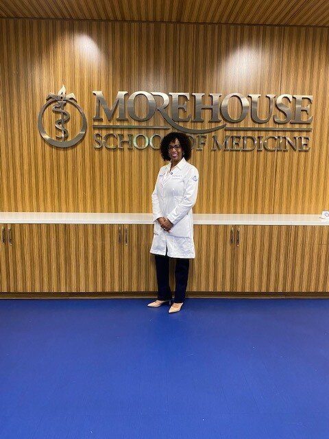 A woman in white lab coat standing in front of a sign.