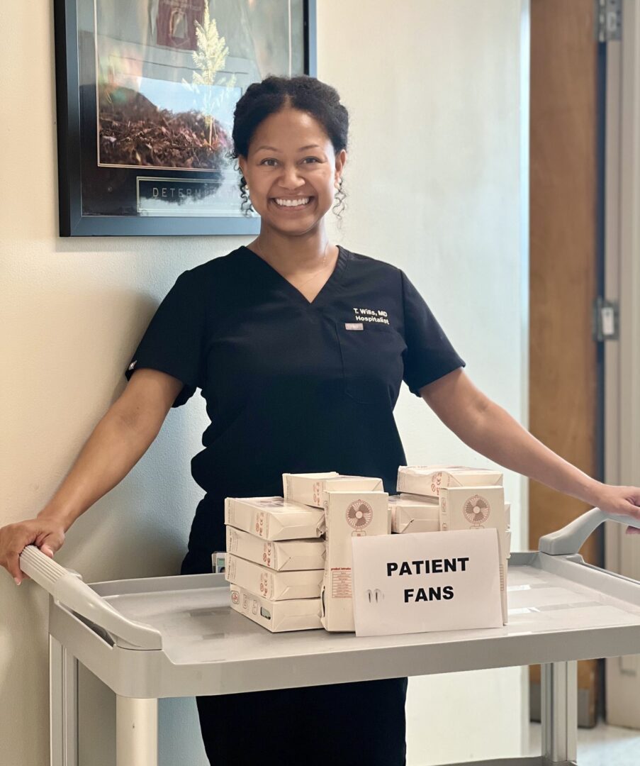 A woman standing next to boxes of patient fans.