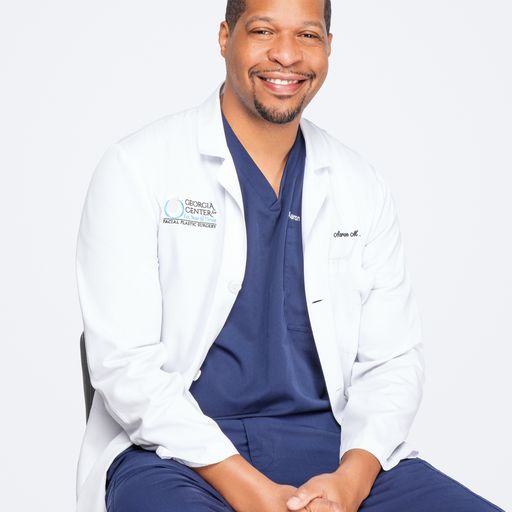 A man in white lab coat sitting on chair.