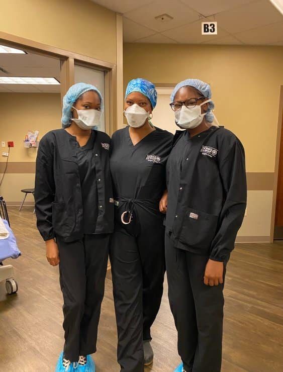 Three nurses in scrubs and masks pose for a picture.