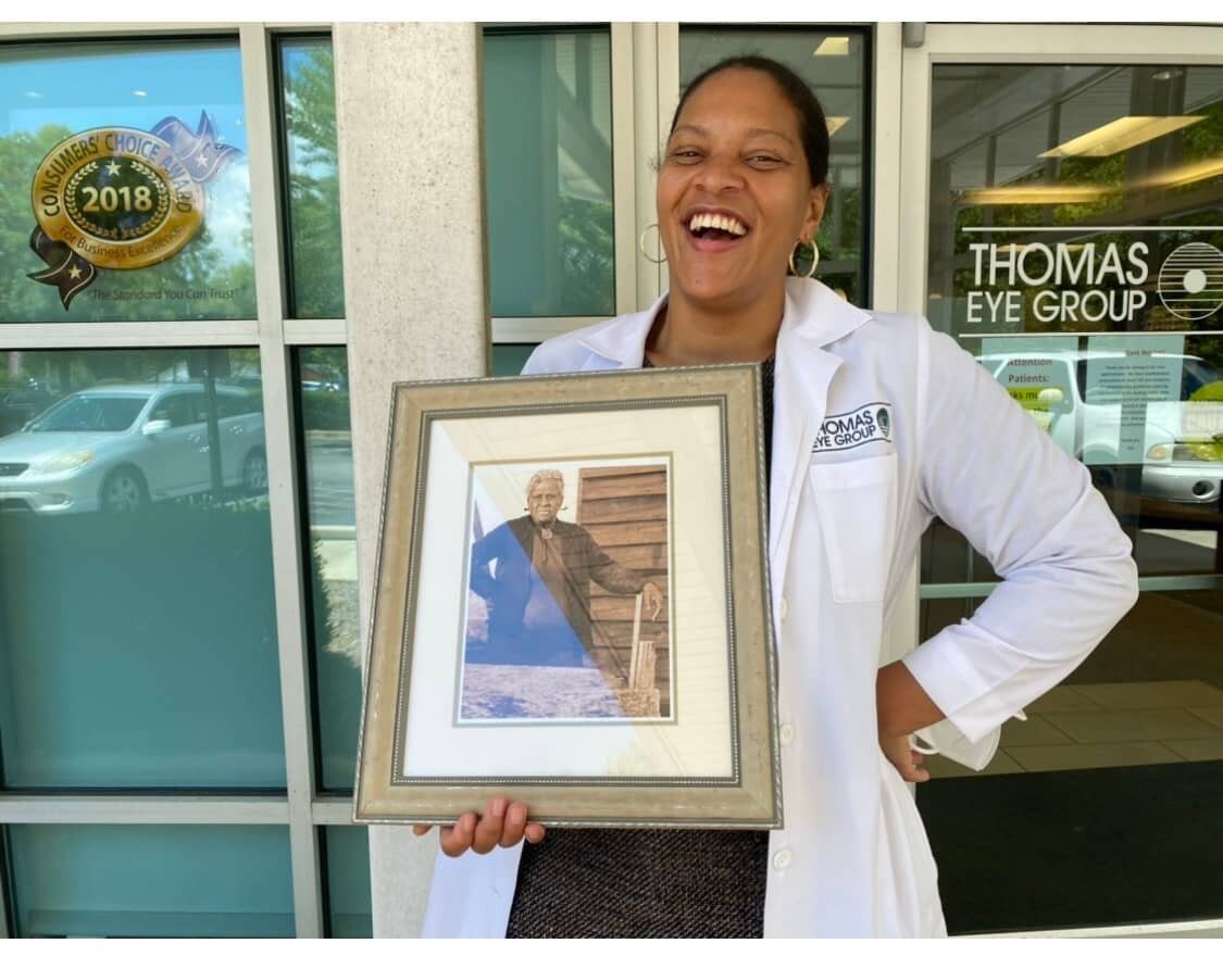 A woman holding up a framed picture outside.