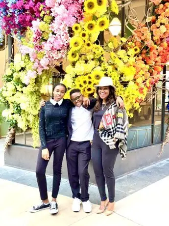 Three women posing for a picture in front of flowers.