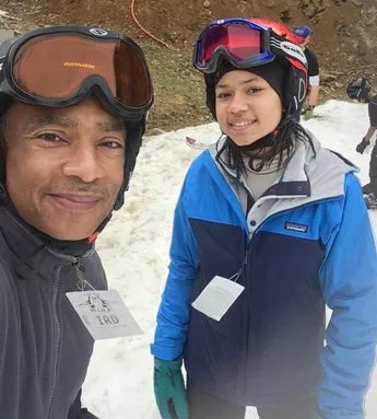 A man and woman in ski gear standing on snow.