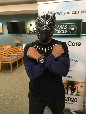 A man in black and white mask holding his hands on the back of his shirt.