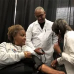 A group of people in lab coats are checking blood pressure.