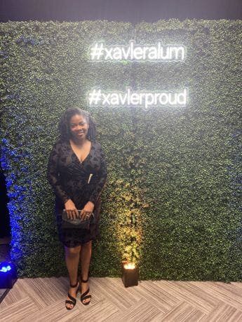 A woman standing in front of a wall with the hashtag # xavieralum