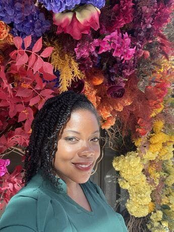 A woman standing in front of flowers and trees.