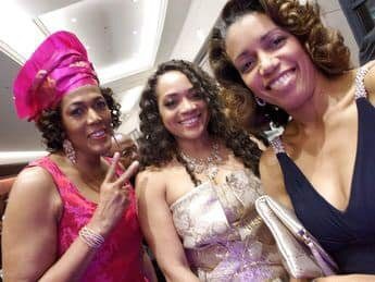 Three women in dresses and a turban pose for the camera.