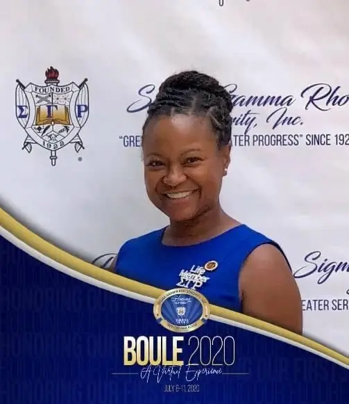 A woman in blue shirt and black pants standing next to a wall.