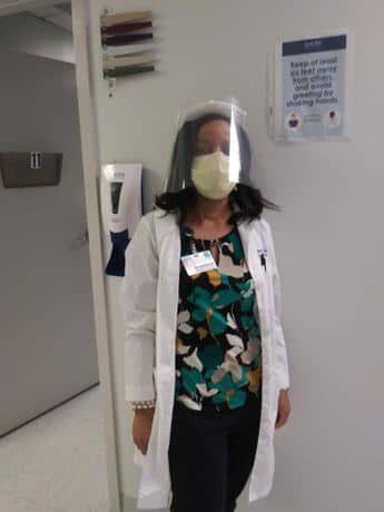 A woman wearing a lab coat and mask standing in front of a door.