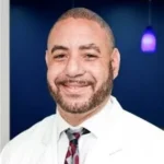A man in white coat and red tie.