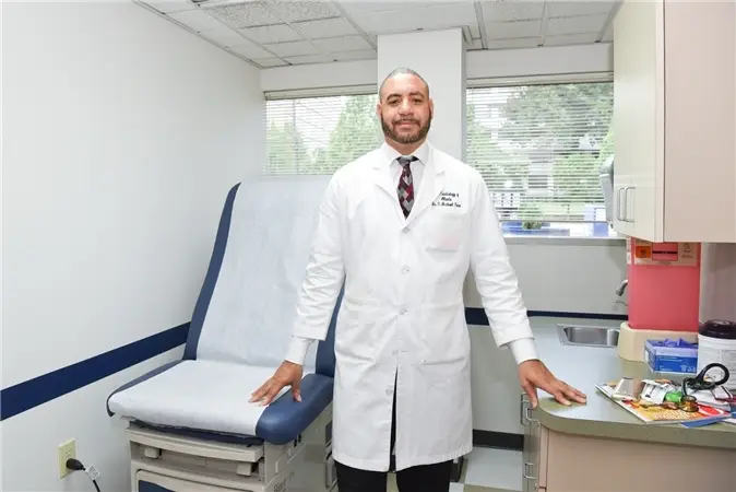 A man in white lab coat standing next to a chair.