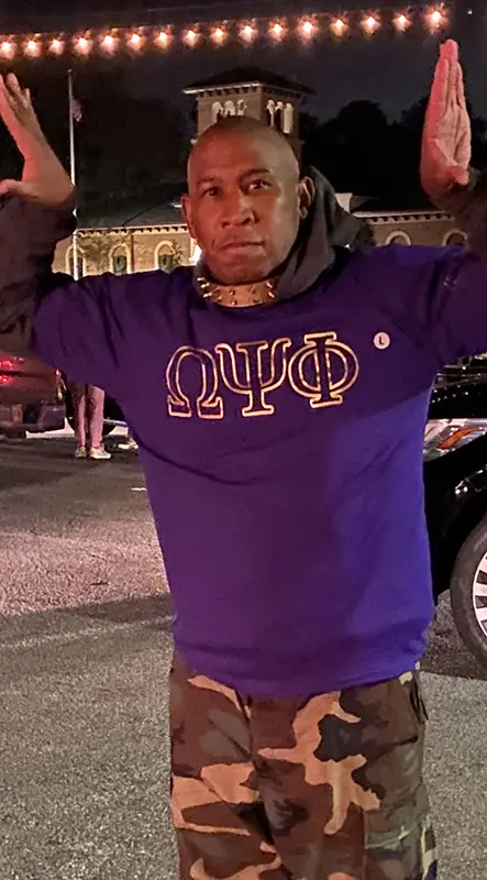 A man in purple shirt and gold letters on it.