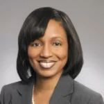 A woman with black hair wearing a gray suit.