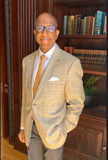 A man in a suit and tie standing next to a book case.