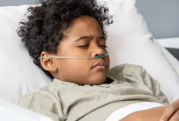 A young boy laying in bed with a tube connected to his nose.