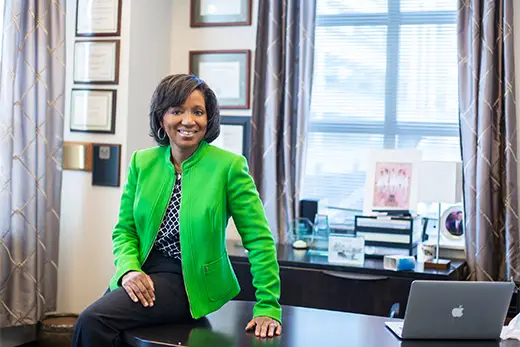 Smiling businesswoman in green jacket at desk.