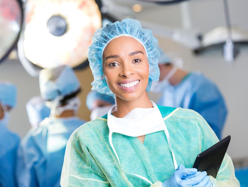 A woman in scrubs and a surgical cap smiles for the camera.