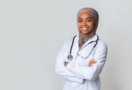 A woman in white coat and head scarf with arms crossed.